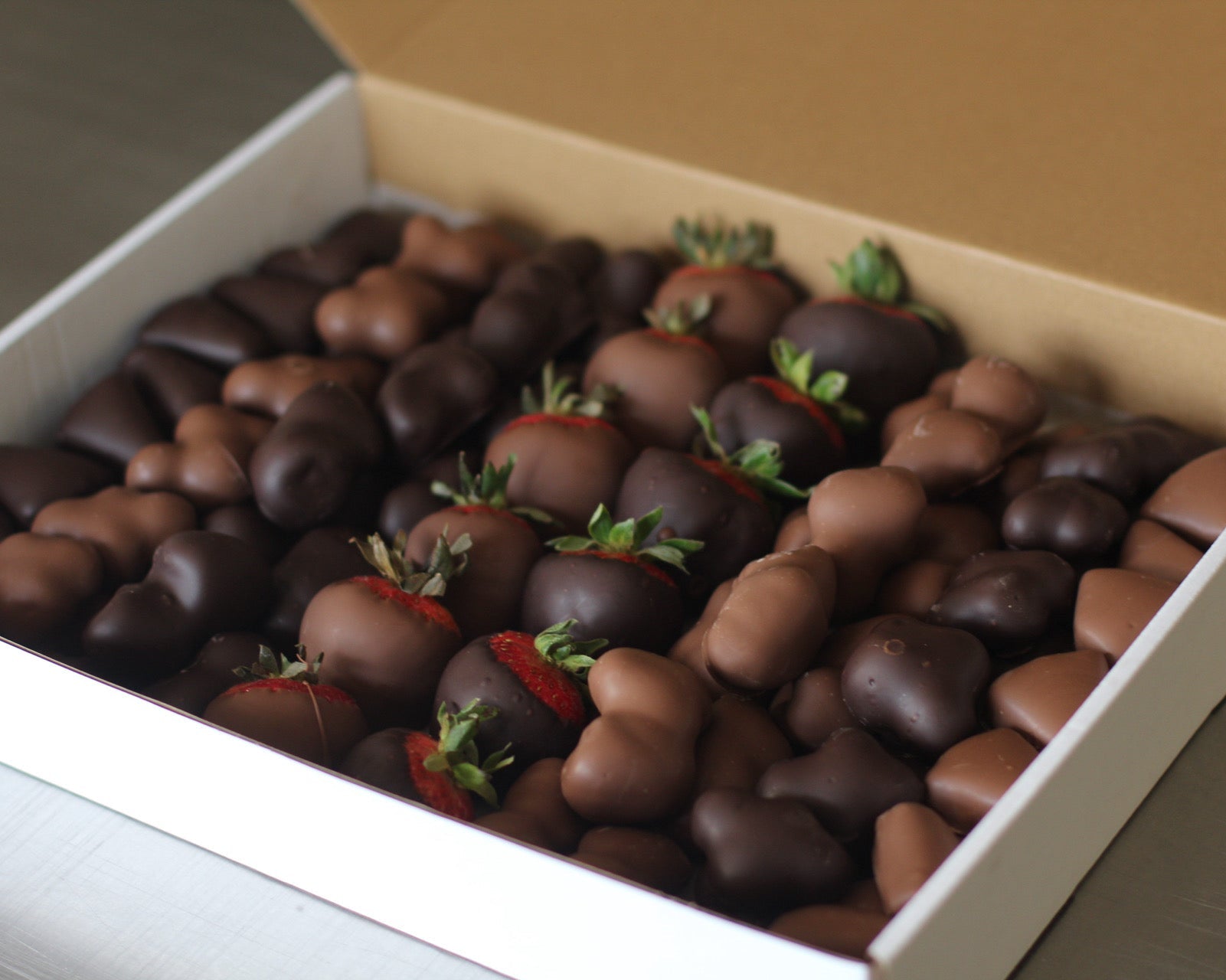 A white box filled with assorted chocolate-covered fruits, including raspberries, blueberries, strawberries, and pineapple.i