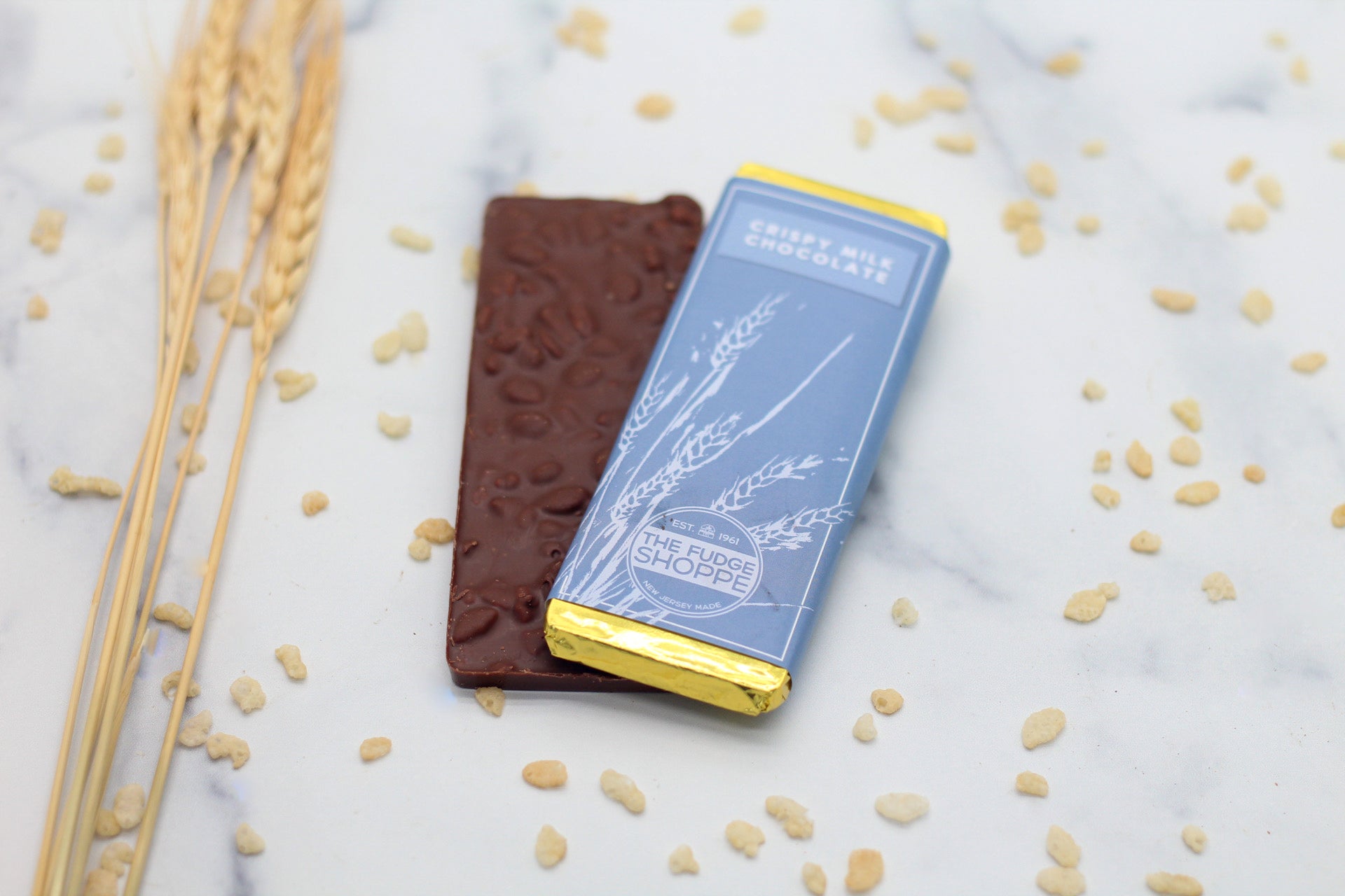 A milk chocolate bar with visible crispy inclusions, presented on a marble surface with decorative elements around.