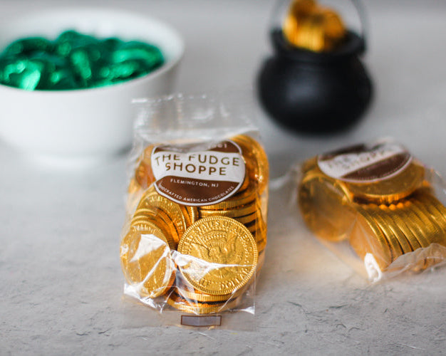 Packaged gold foiled coins on a table, with a bowl of green candy in the background.