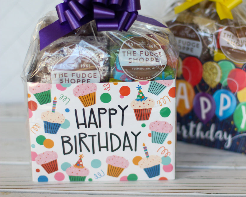 Two gift boxes from The Fudge Shoppe with 'Happy Birthday' labels on a wooden surface.