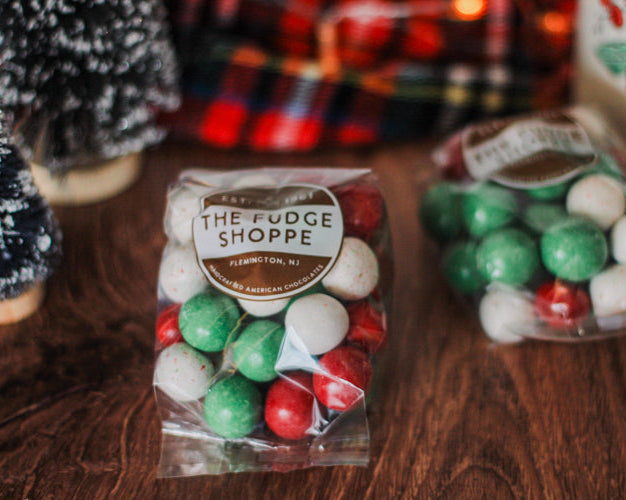 Christmas-themed malt balls with 'The Fudge Shoppe' label on a wooden surface.