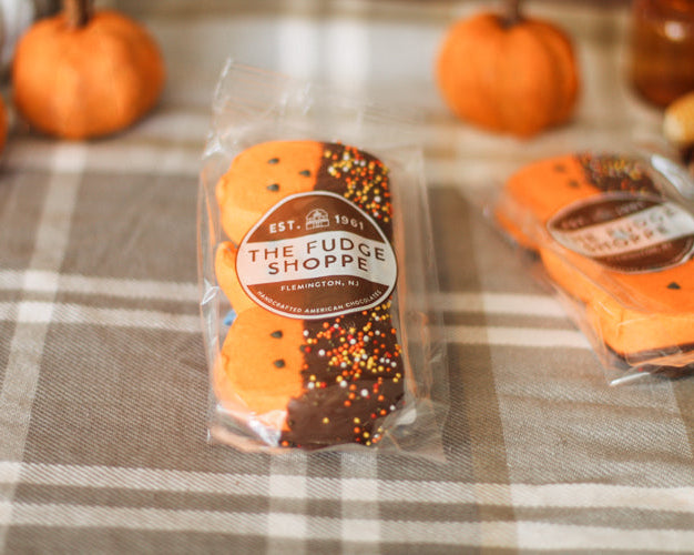 Packaged Halloween-themed marshmallow pumpkins with 'The Fudge Shoppe' label on a plaid tablecloth.