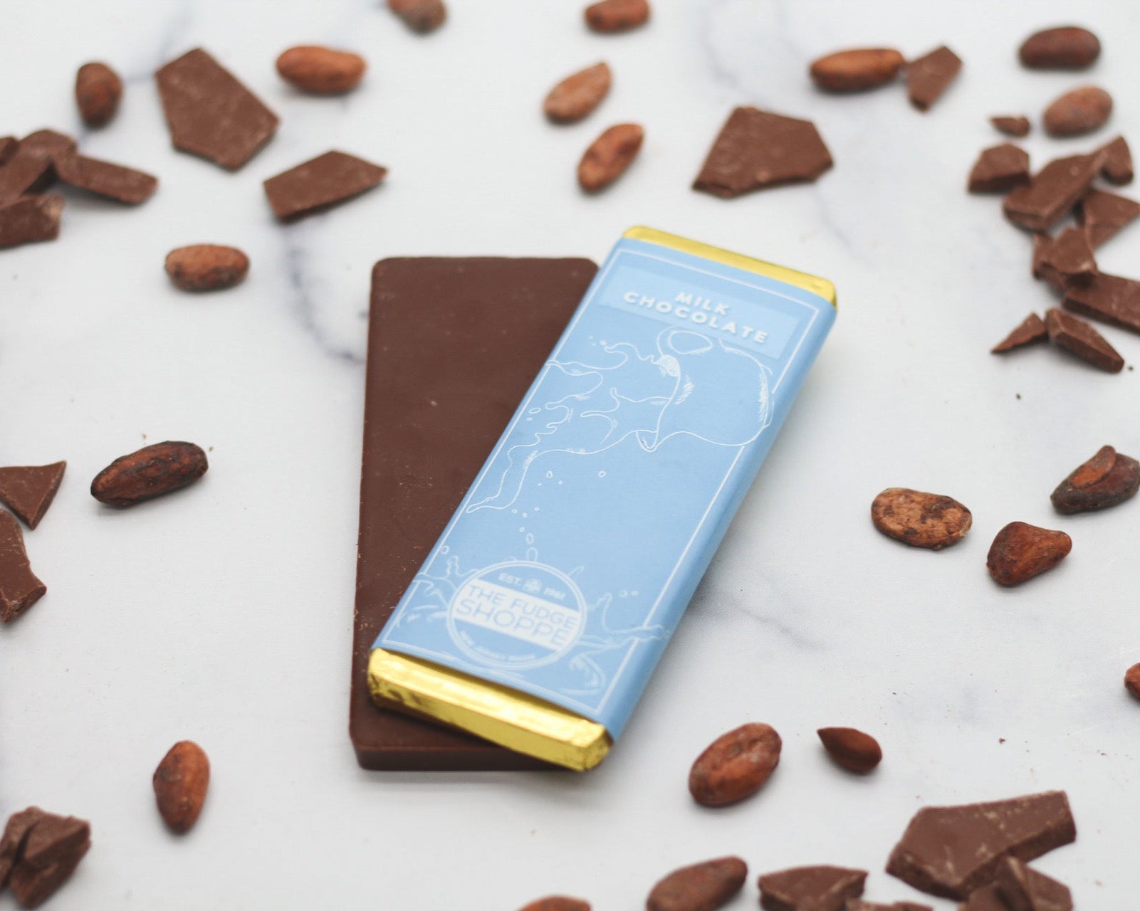 A milk chocolate bar with a gold wrapper, placed on a surface with scattered chocolate chips and pieces of chocolate.