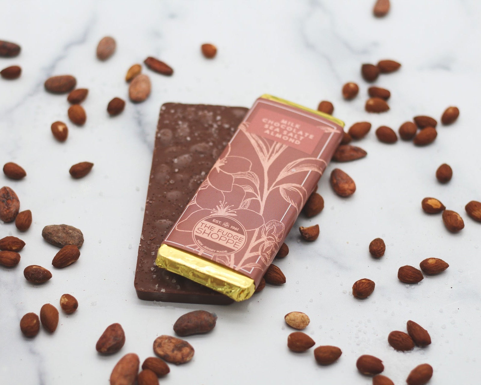 A milk chocolate sea salt almond bar positioned on a marble surface, surrounded by scattered roasted almonds.