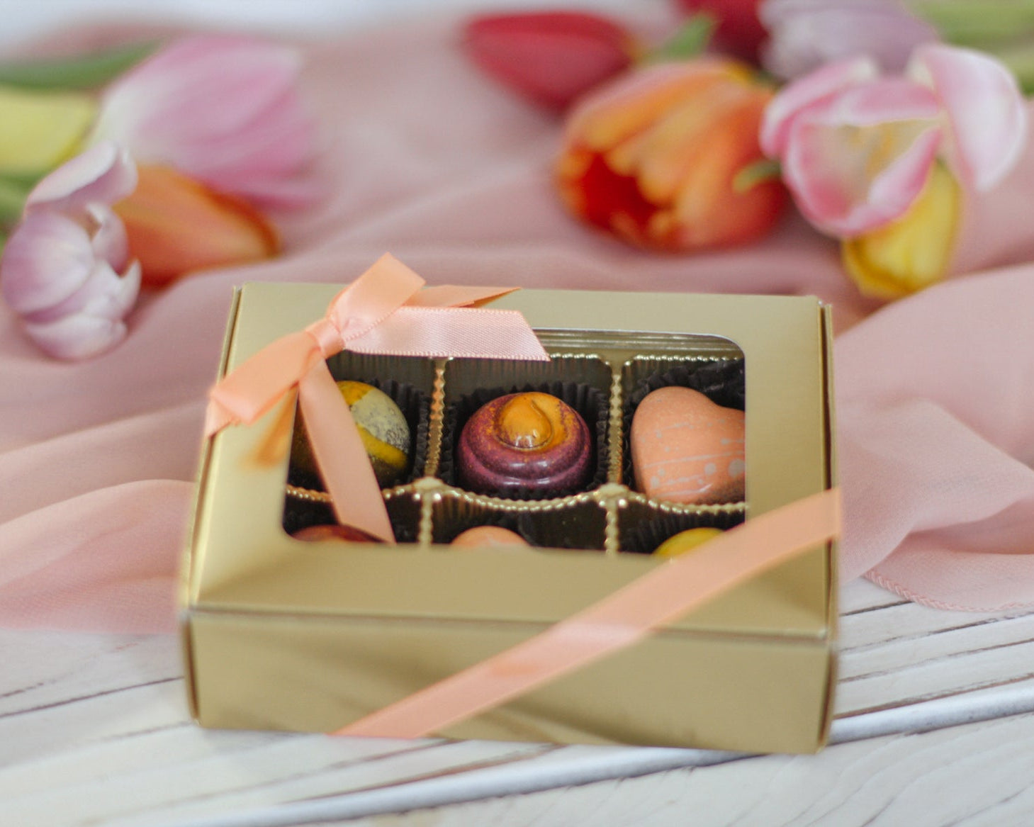 Gold box of liquor truffles with a pink ribbon on a floral background