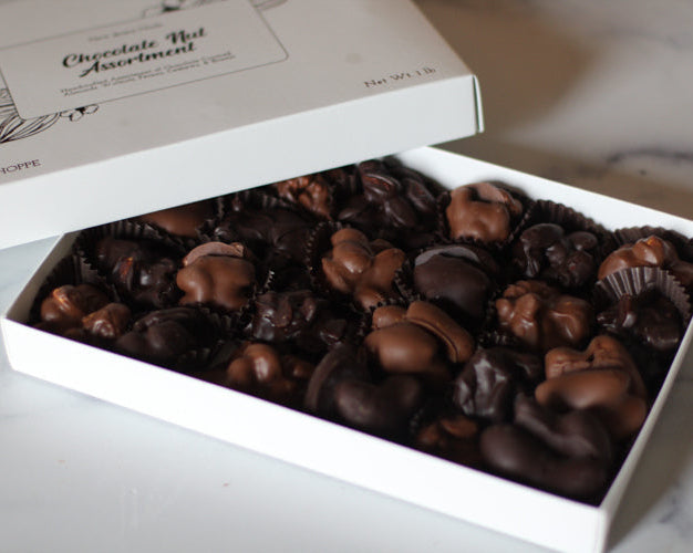 A box of chocolate covered nuts, including almonds, walnuts, pecans, and cashews, arranged neatly in a gift box.