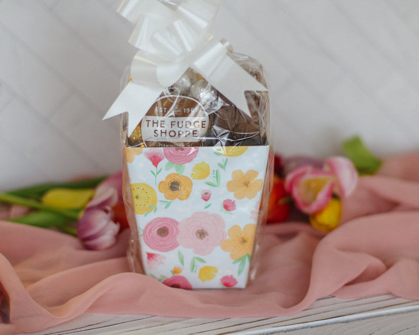 Small floral gift box wrapped in floral paper with a white bow on a pink fabric background