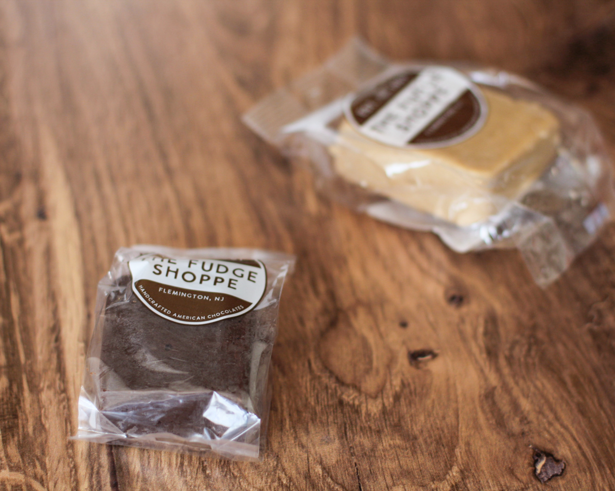 Two individually wrapped chocolate fudges on a rustic wooden tabletop