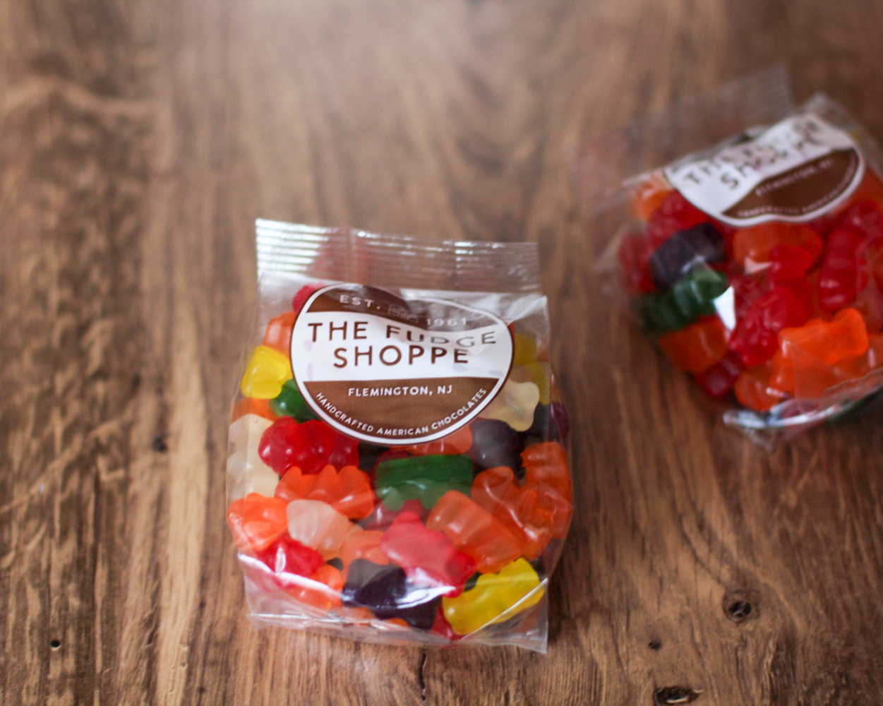 Two clear plastic bags filled with assorted colorful gummy candies sit on a rustic wooden tabletop.