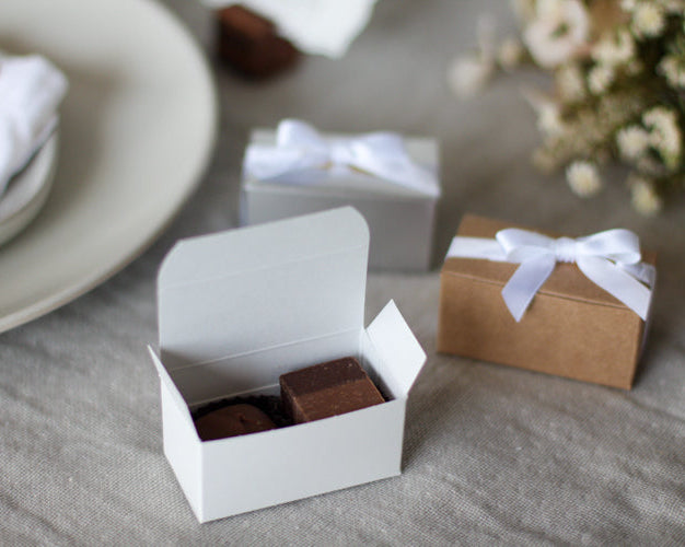 Small white box with a brown square inside, placed on a textured surface with another similar box and a small brown box in the background.