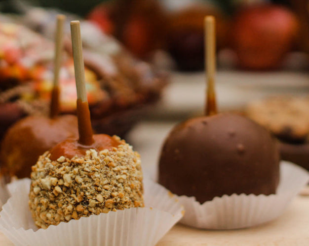 Caramel apples with different dips, including chocolate and peanuts, on a table with fall decorations in the background.
