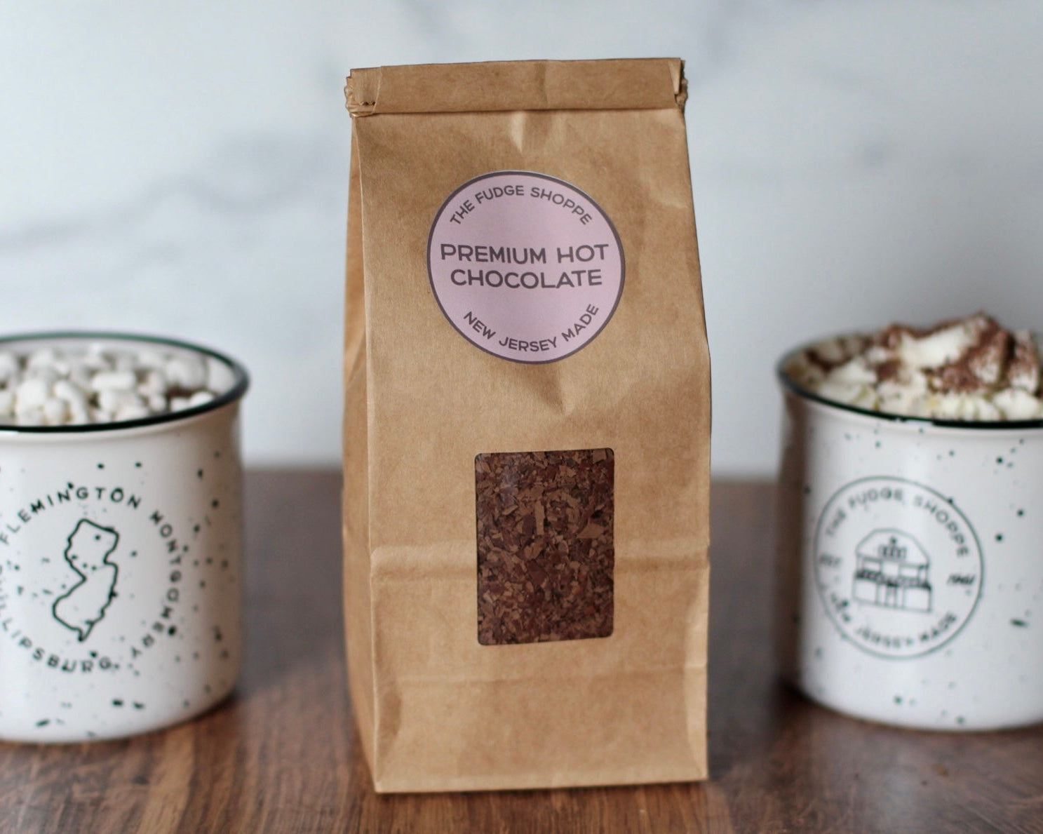 A package of premium hot chocolate mix standing in front of two cups of hot cocoa with mini marshmallows on top.