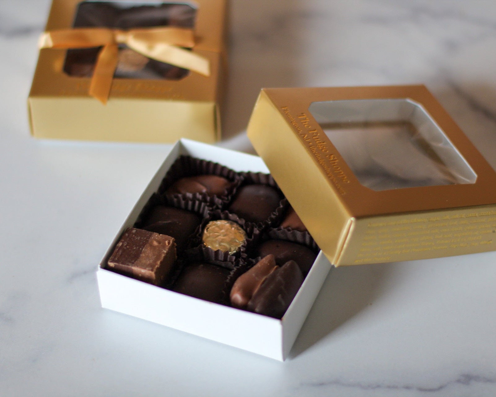 A small square box of assorted chocolates, with some chocolates visible through the box window, placed on a marble surface.