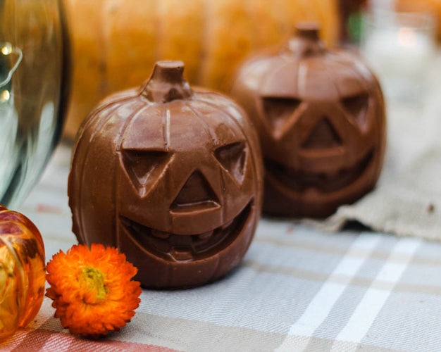 Chocolate jack o' lantern shaped like a carved pumpkin on a table with fall-themed decorations around it.