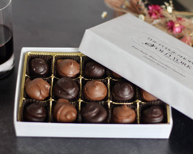 wine soaked cherries coated in chocolate in a white box with wine in background