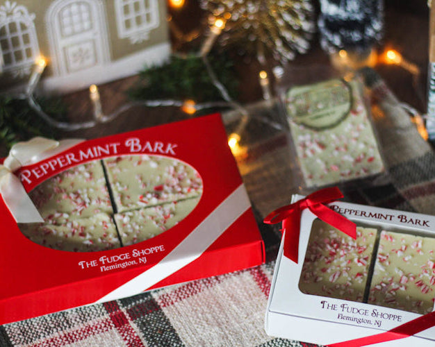 Packaged peppermint bark with red and green accents on a festive table, presented in a box and decorated with Christmas-themed decorations in the background.