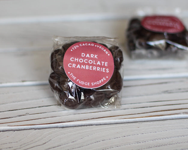 Packaged dark chocolate cranberries with a pink label on a wooden surface