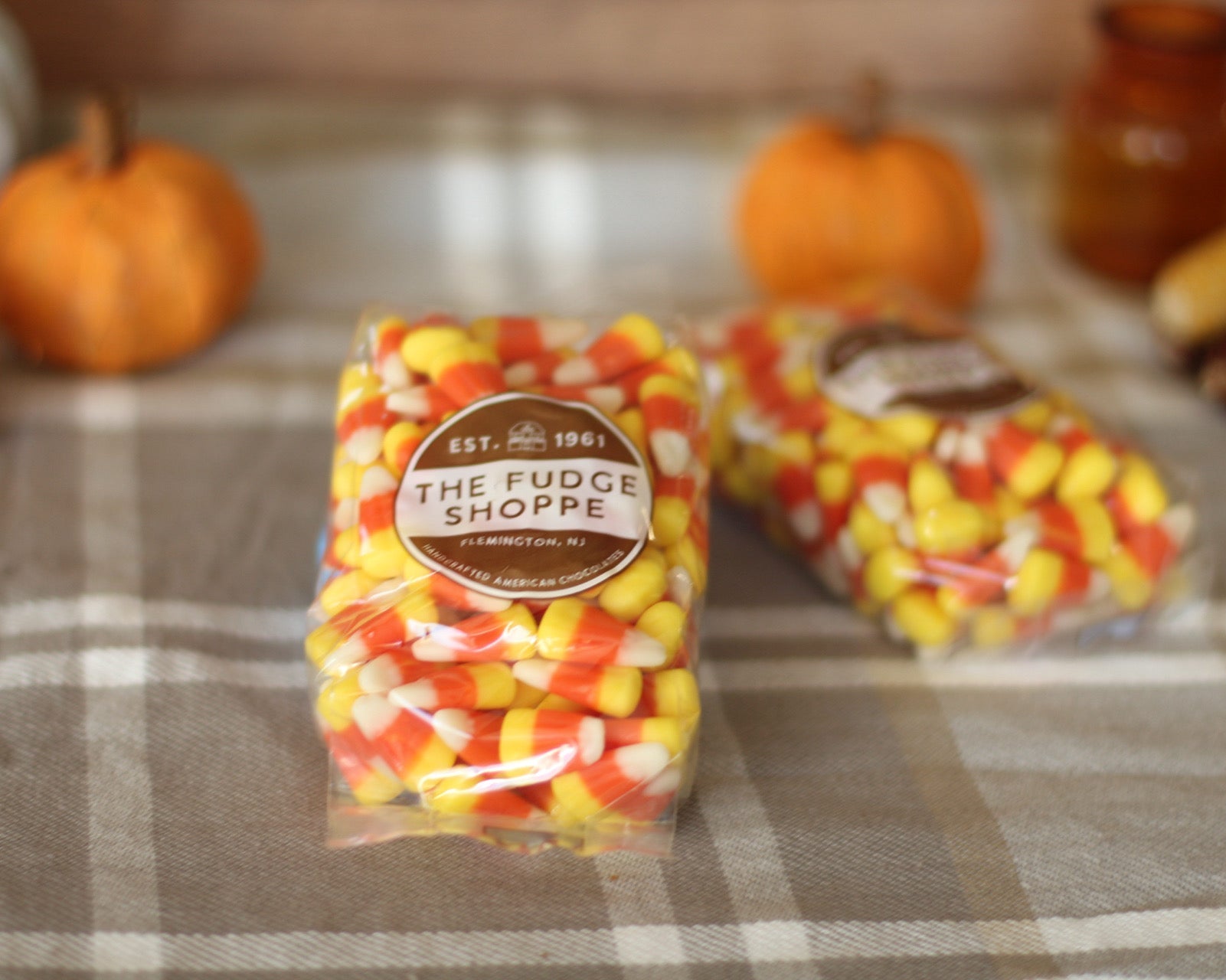 Packaged candy corn on a plaid surface with pumpkins in the background.