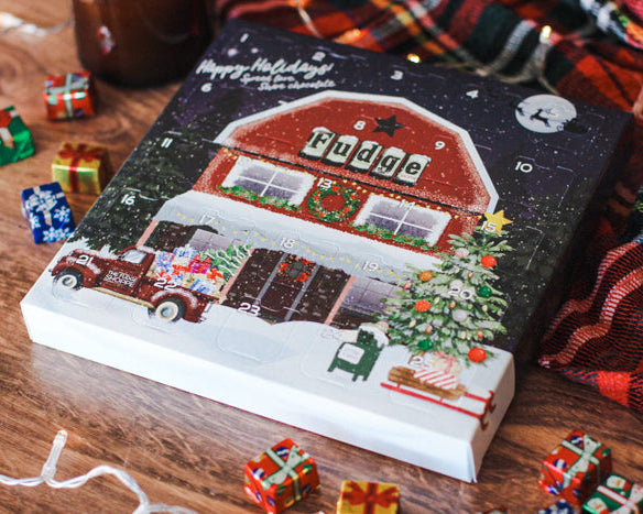 An advent calendar depicting a Christmas themed scene with a red and white building, foil wrapped chocolates, and festive decorations.