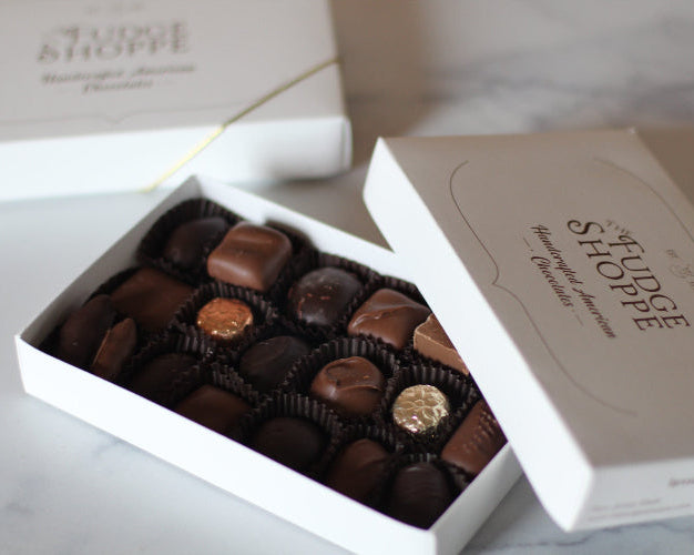 An open box of assorted chocolates from The Fudge Shoppe, displaying a variety of chocolate candies.