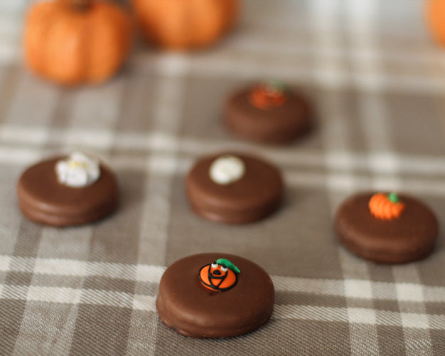 Chocolate oreos decorated like pumpkins on a plaid fabric background