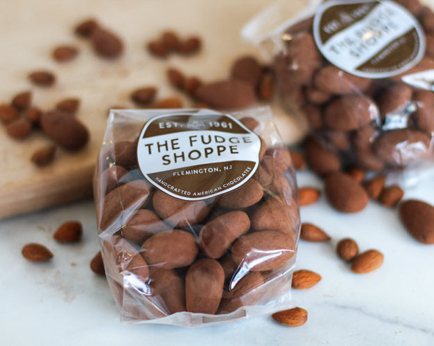 Packaged almonds from The Fudge Shoppe on a marble surface with scattered almonds.