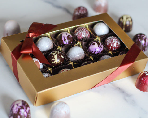 A box of assorted coffee flavored truffles, with a variety of colors and toppings on the truffles, presented in a gold and red box.