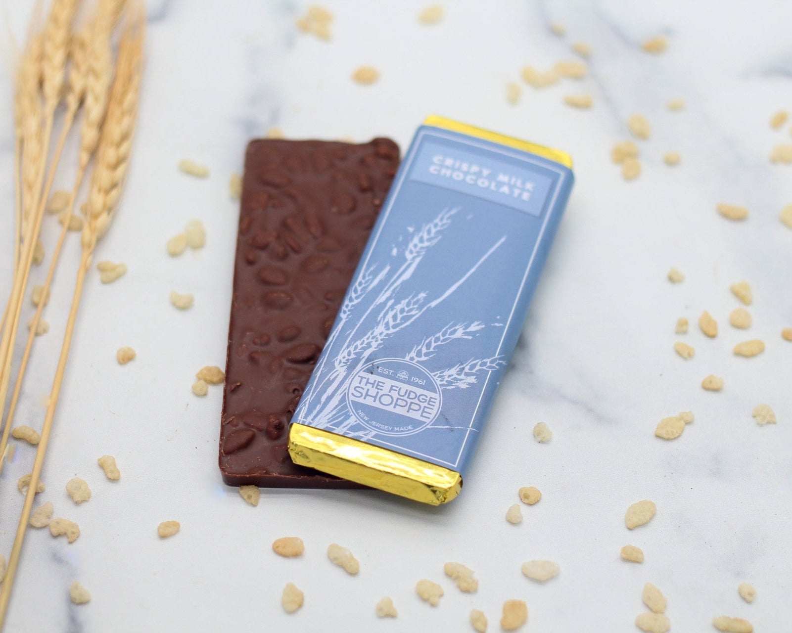 A milk chocolate bar with visible crispy inclusions, presented on a marble surface with decorative elements around.