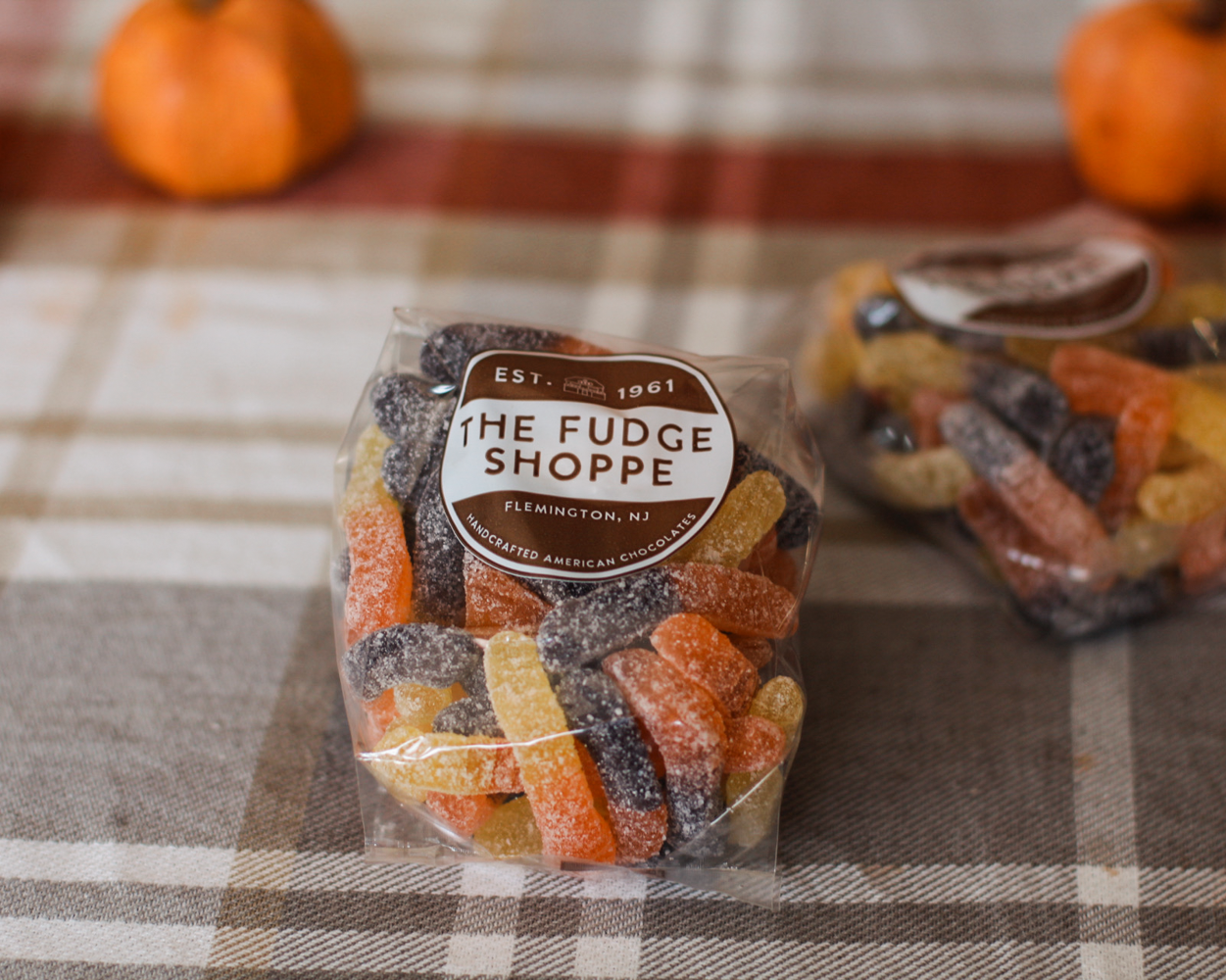 Two clear bags of assorted gummi worms 
in a brown and beige plaid blanket, with small pumpkins blurred in the background.