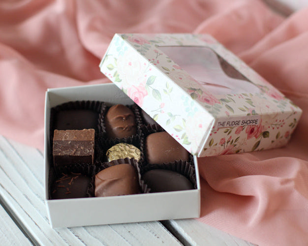 A small open box of assorted chocolates with various shapes and toppings, placed on a soft pink velvet surface.