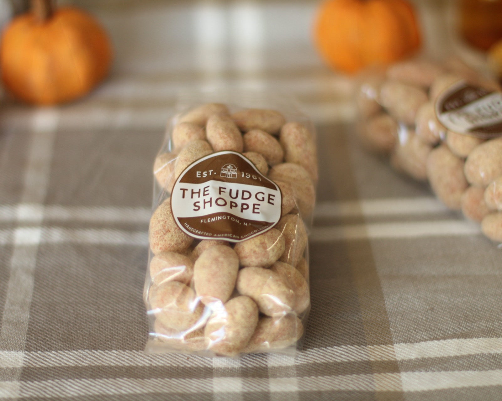 Packaged peanuts with 'The Fudge Shoppe' label on a checkered tablecloth with pumpkins in the background.