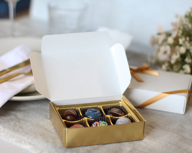Gold box of chocolates on a marble surface with a white napkin and gold utensils.
