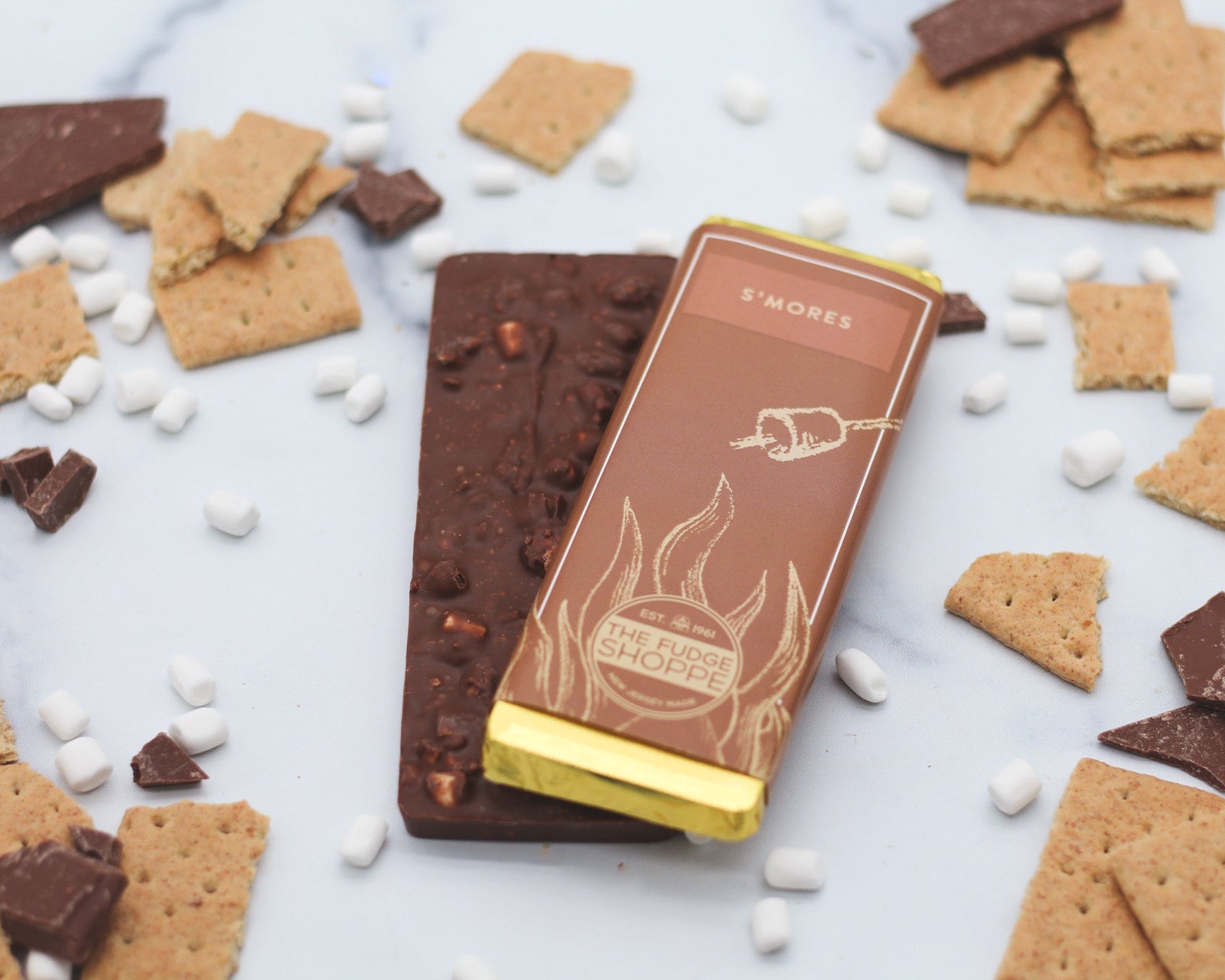 A smores bar surrounded by crushed graham crackers and mini marshmallows on a marble surface.