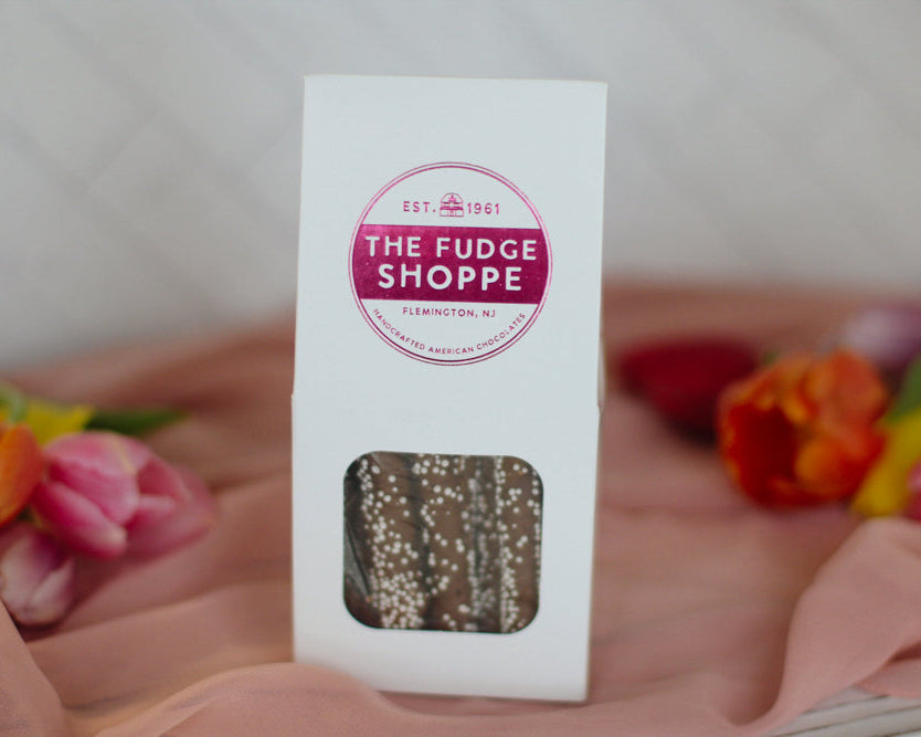 Box of sprinkle pretzel sticks from The Fudge Shoppe with flowers in the background