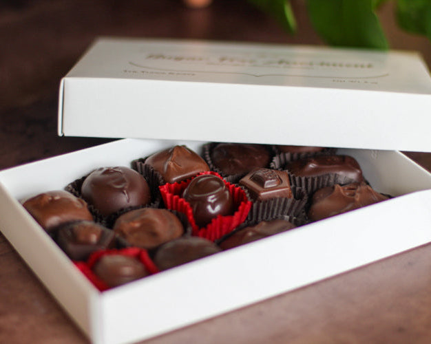 Open box of chocolates with a white lid on a wooden surface