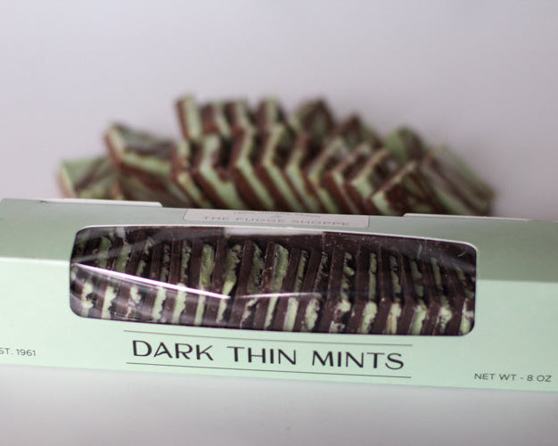 A box of Dark Thin Mints chocolate-mint squares with multiple mint leaves scattered around.