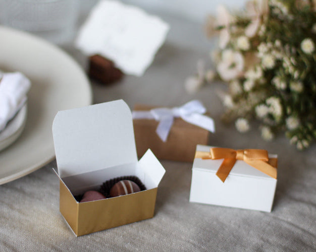 Small gift boxes with ribbons on a table setting with a plate and flowers.
