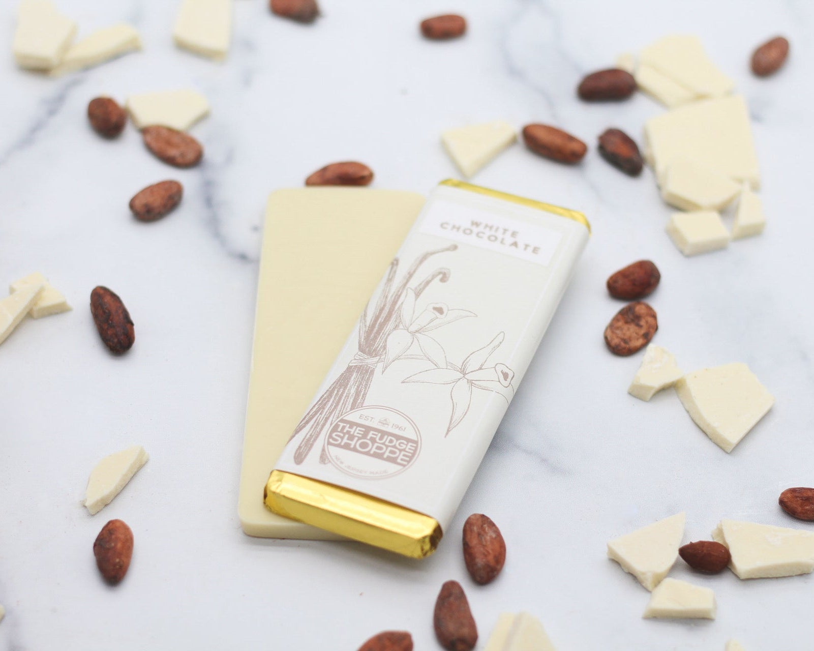A white chocolate bar with a golden wrapper, resting on a marble surface surrounded by crumbled white chocolate pieces.