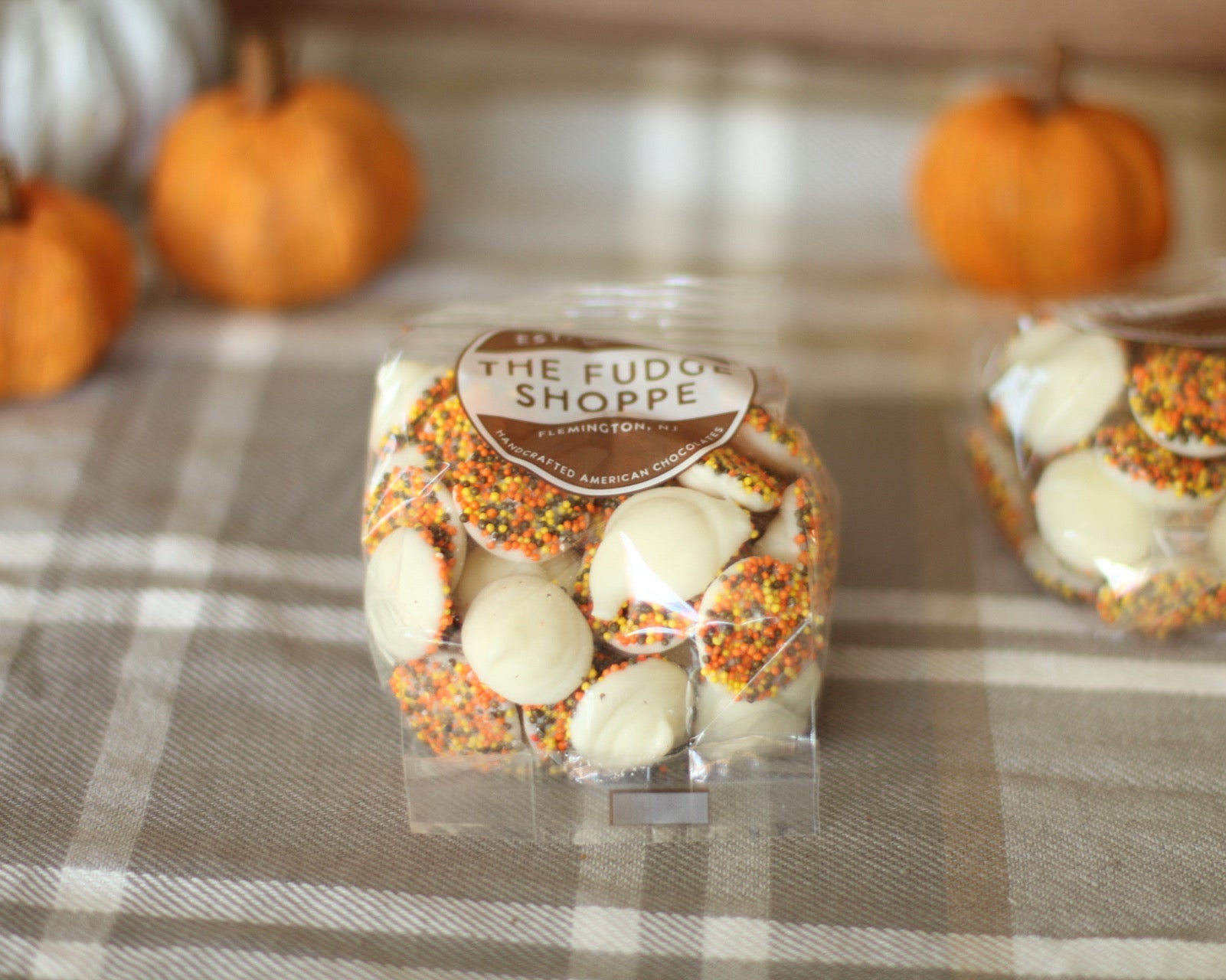 Packaged white non pareils with a label on a checkered tablecloth with pumpkins in the background