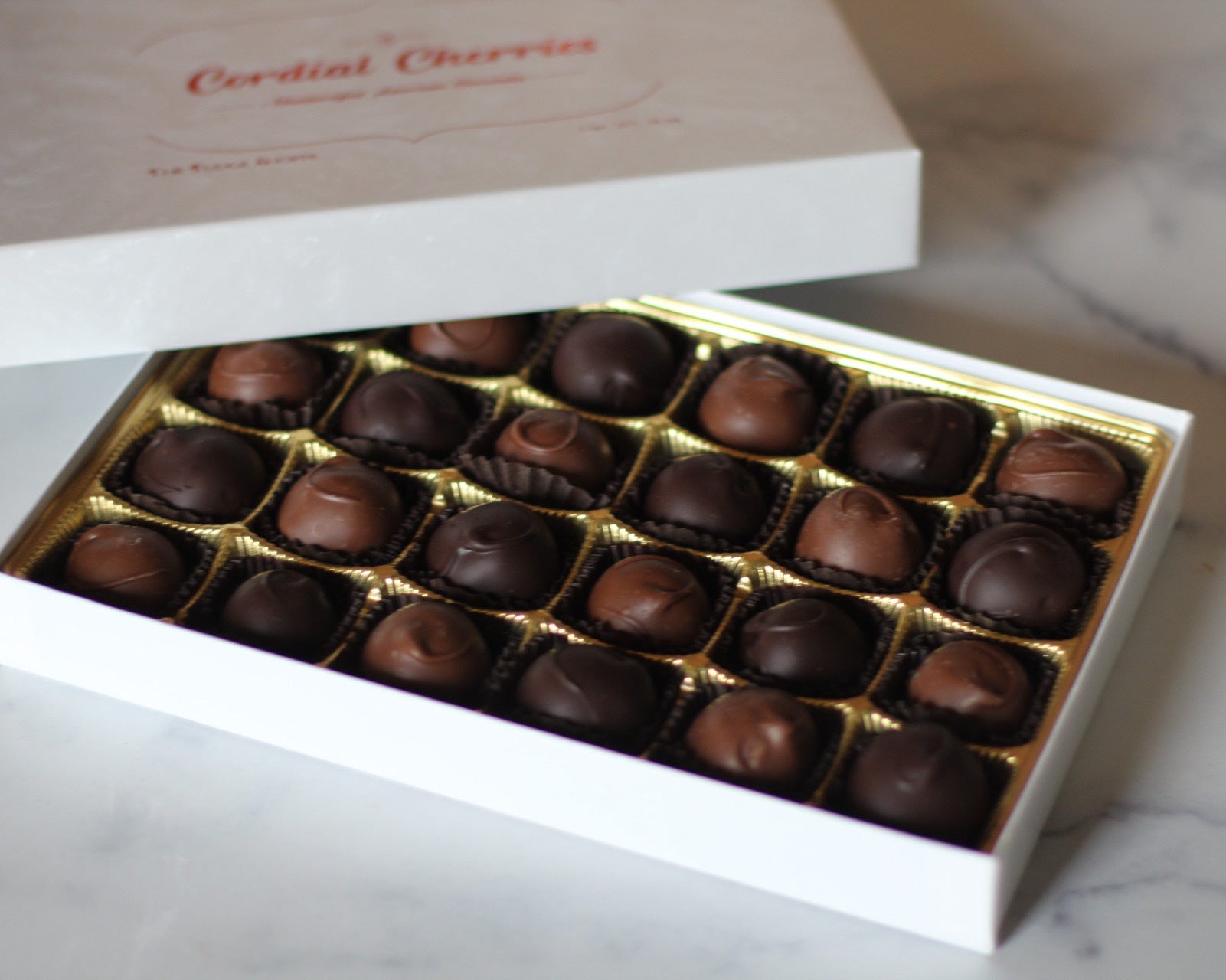 A box of chocolate cordial cherries in a white gift box with the words 'Cordial Cherries' written on the lid.
